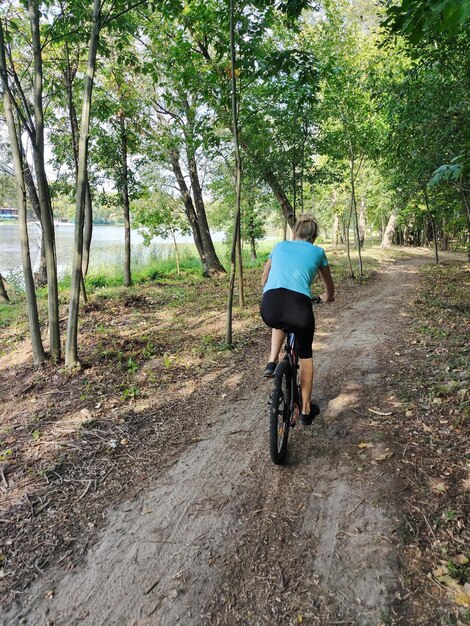 写真 若い金の女性が川の近くの森で自転車に乗っています