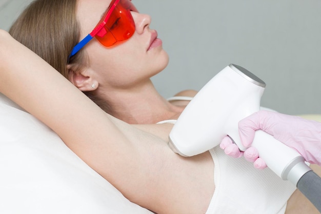 Фото Молодая блондинка проходит процедуру лазерной эпиляции подмышек в салоне красоты.