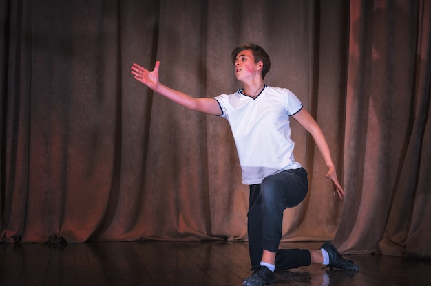 Фото Молодой мальчик-танцор репетирует на сцене элементы танца. эмоции в хореографии