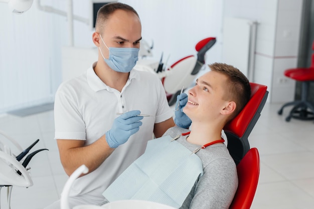 若い歯科医は、現代の白い歯科のクローズアップで若い男の歯を調べて治療します歯科補綴物の治療と歯のホワイトニング現代の歯科予防