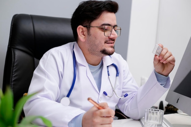 사진 젊은 의사가 진료소에 앉아서 약을 손에 들고 있다