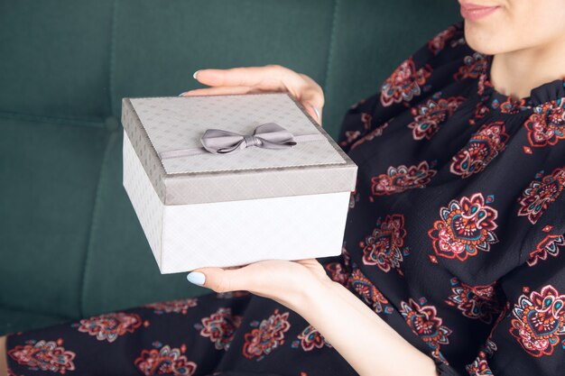 Фото Молодая девушка в платье с подарочной коробкой сидит на диване