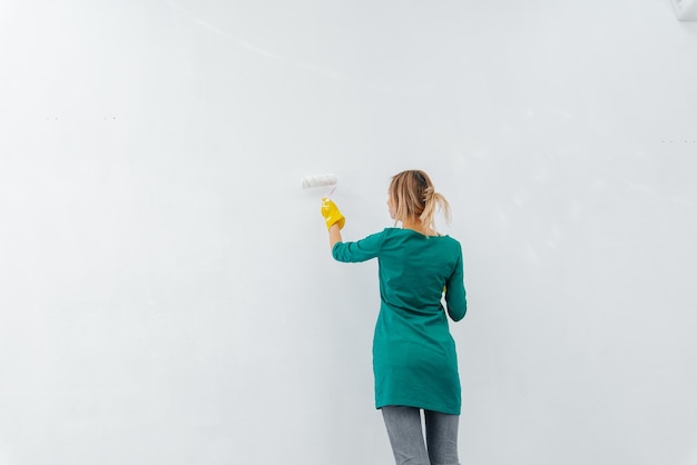 Фото Молодая девушка занимается ремонтом и красит валиком белую стену в новой квартире ремонт интерьера и новая квартира новоселье и желанная ипотека