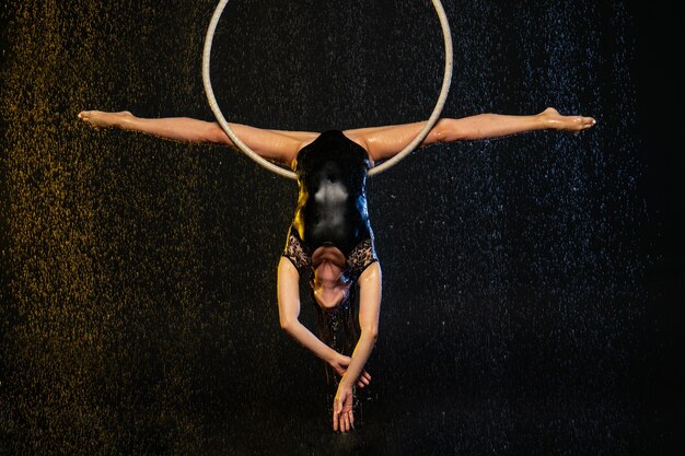 Фото Молодая девушка выполняет акробатические элементы на воздушном ринге. аква студия съемки спектаклей на черном фоне.