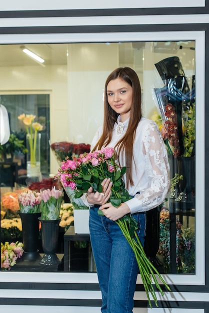 写真 居心地の良いフラワーショップを背景に美しいお祭りの花束でポーズをとる少女フローリストリーとフラワーショップでの花束作り中小企業