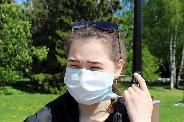 写真 パンデミックの最中、公園で暖かく明るい晴れた日に、若い女の子が外のウイルスから医療用保護マスクを着用します。