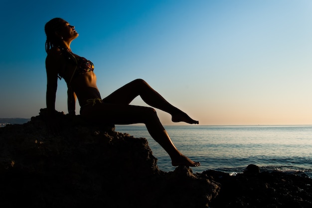 사진 어린 소녀가 돌 위에 앉아 바다와 일출의 전망을 즐긴다