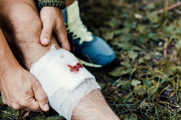 写真 包帯を巻いた観光客の若い男がキャンプに行く途中で足の怪我を包帯で包む