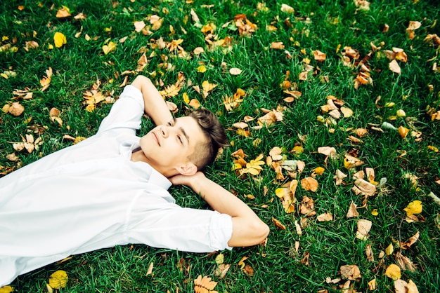 白いシャツを着た若い男が紅葉と草の上にあります。