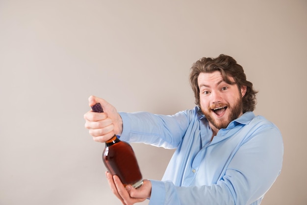 Фото Молодой счастливый бородатый мужчина с бутылкой коньяка на светло-сером фоне