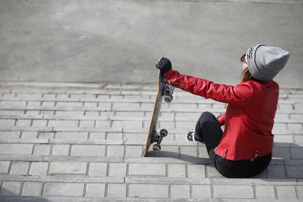 사진 젊은 힙스터 소녀가 스케이트보드를 타고 있다 스케이트보드를 타고 도시를 산책하는 여자 친구 스케이트보드를 들고 거리에서 봄 스포츠