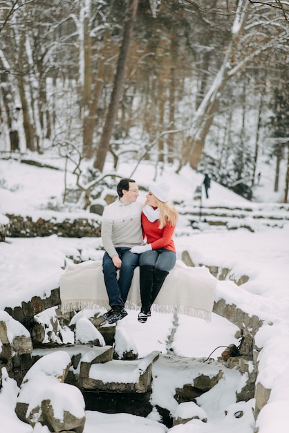 冬のジャケットとスカーフが雪の公園に座っている若い恋人のカップル