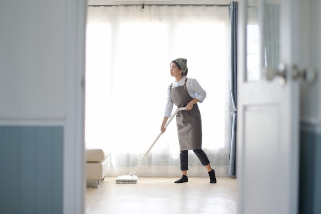 写真 モップで家を掃除する若いメイドキッチンの背景があります