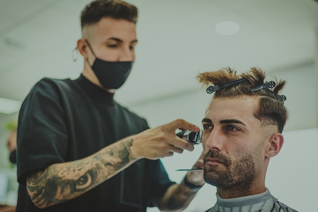 写真 入れ墨の腕を持つ若い男は理髪店で男の髪をカットします