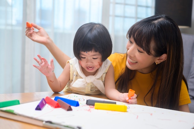 사진 집에 있는 거실에서 딸이 색연필로 그림을 그리는 것을 돕는 젊은 엄마.