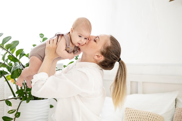 写真 明るい寝室で生まれたばかりの小さな赤ちゃんを腕に抱く若い母親がキスをし、母親と赤ちゃんに対する母親の愛と世話を称賛する