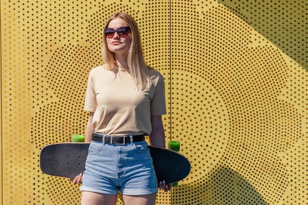 Фото Молодая красивая блондинка со скейтбордом на желто-синем фоне