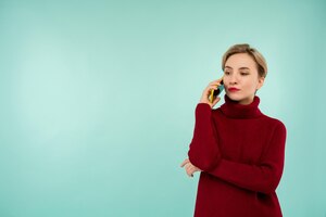 Фото Молодая серьезная женщина в красном свитере со смартфоном на синем фоне