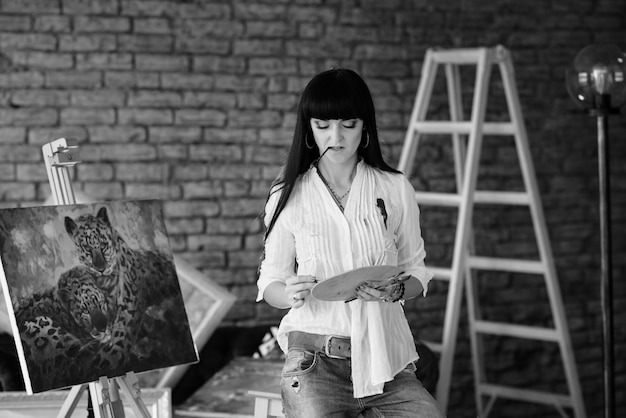 Фото Молодой улыбающийся брюнетка женщина художник в своей студии держит кисть.