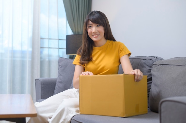 Молодая улыбающаяся женщина, открывающая картонную коробку в гостиной дома