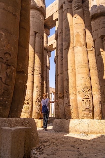 エジプト、ルクソール神殿の柱に描かれたエジプトの絵を見ている若い観光客