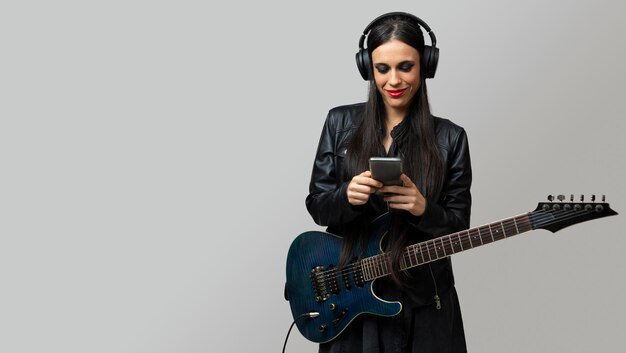 写真 若い女性ギタリストがワイヤレスヘッドフォンと携帯電話で音楽を聴くことを楽しんでいます