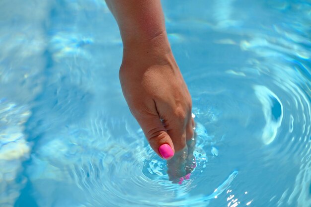 写真 若い女性の手がプールの澄んだ青い水に触れる 美しい明るい夏の日