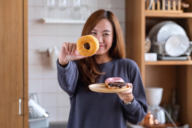 写真 自宅のキッチンでドーナツを持って見せている若い女性