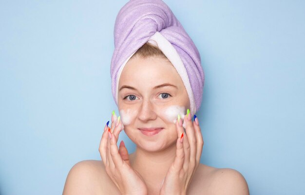 Фото Молодая женщина в полотенце на голове моет волнистую пену для мытья щек