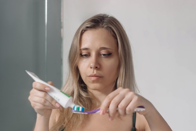写真 歯ブラシで歯磨きをするためのチューブから歯磨き粉を圧縮している若い女性