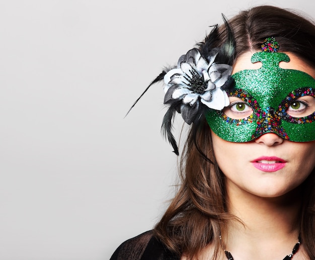 Фото Молодая женщина в карнавальной маске поверх серого