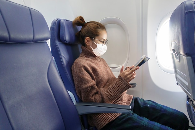 Молодая женщина в маске путешествует на самолете, новое нормальное путешествие после концепции пандемии covid-19