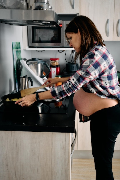 사진 임신이 매우 진행된 젊은 여성이 요리를 하고 있습니다.