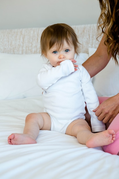 aadorable baby sitting on a bed with a brunette woman chewing her sleeve