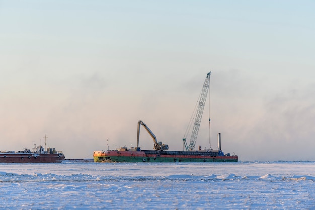 Aak met kraan. Baggerschip aan het werk op zee. Zonsondergang in de Arctische zee. Bouw Marine offshore werken. Dambouw, kraan, schuit, baggerschip.