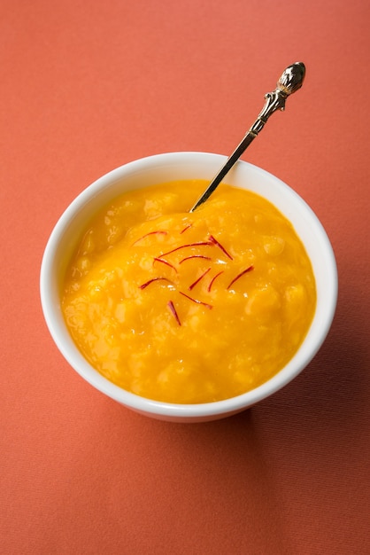 aam ras is a delicious indian seasonal dessert recipe,  aamras is plain haapus or alphonso mango puree or pulp with saffron, kesar topping. served in a terracotta bowl over colourful background.