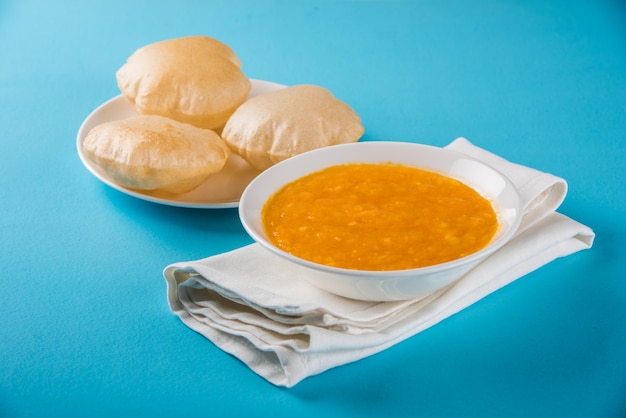 Aam Ras Puri is a delicious Indian recipe served as a seasonal Dessert,  Aamras is plain Mango Puree or Pulp, Served in a ceramic bowl and plate over colourful or wooden background. Selective focus