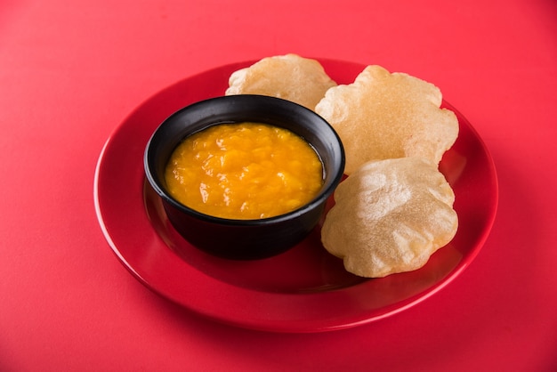 Aam Ras Puri is a delicious Indian recipe served as a seasonal Dessert,  Aamras is plain Mango Puree or Pulp, Served in a ceramic bowl and plate over colourful or wooden background. Selective focus