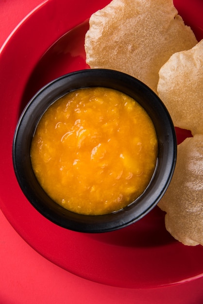 Aam Ras Puri is a delicious Indian recipe served as a seasonal Dessert,  Aamras is plain Mango Puree or Pulp, Served in a ceramic bowl and plate over colourful or wooden background. Selective focus