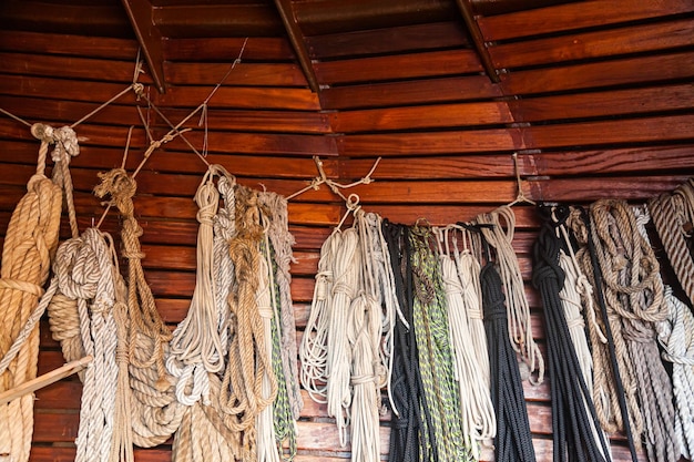 Aan de houten wand van een oud schip hangen veel verschillende touwen die opgerold zijn vastgebonden