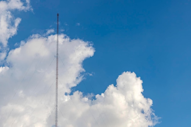 Aan de linkerkant van de afbeelding bevindt zich een radioantenne van een stalen frame met een sling aan de grond bevestigd. De achtergrond is een helderblauwe lucht met witte wolken. Er is een kopieerruimte aan de rechterkant.