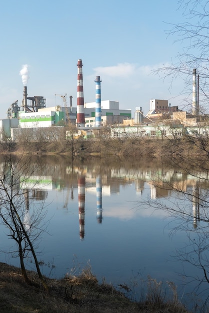 Aan de oever van de rivier staat een grote fabriek Er ontsnapt giftige witte rook uit de schoorstenen van de fabriek Het risico van een milieuramp Weerspiegeling in het water van de rivier van de fabriek