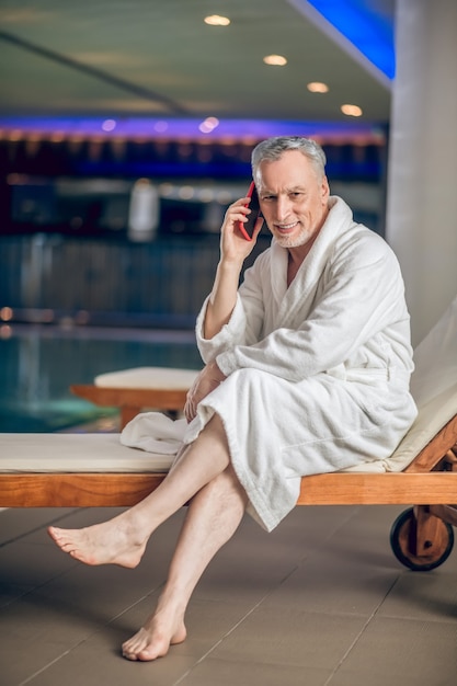 Aan de telefoon. Bebaarde man in een witte badjas in het spacentrum aan de telefoon