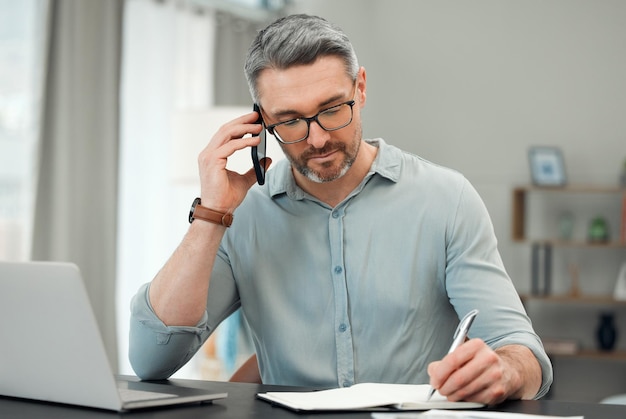 Aan de telefoon met zijn privébankier Bijgesneden opname van een knappe volwassen man die aan het bellen is terwijl hij aan zijn financiën aan een bureau thuis werkt