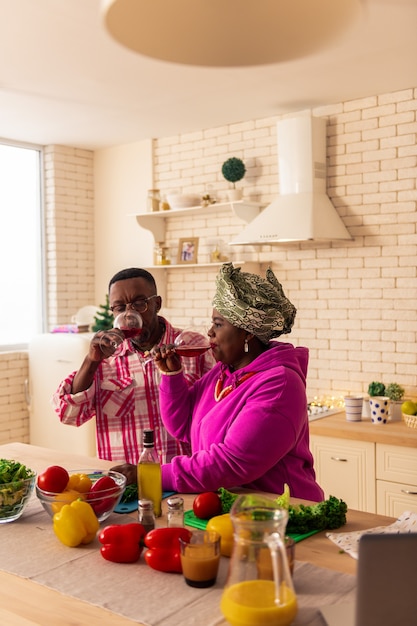 Aan ons. Vrolijke gelukkige paar zittend aan tafel terwijl juichen met wijnglazen