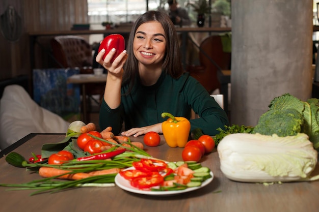 Aan tafel met groenten pakt vrouw een rode paprika