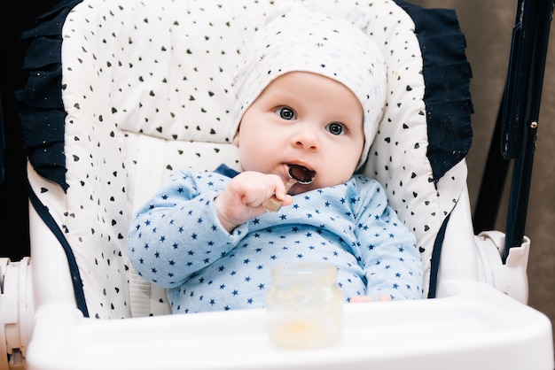 Aanbiddelijk babykind dat met een lepel als hoge stoel eet