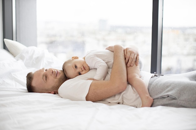 Aanbiddelijk babymeisje dat zacht aan vader op wit bed knuffelt