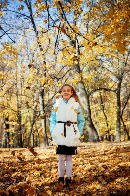 Aanbiddelijk gelukkig meisje dat zich onder de gevallen gekleurde herfstbladeren bevindt die in het de herfstpark spelen