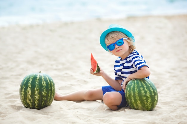 Aanbiddelijk jong geitje bij de kust die sappige watermeloen eet. Vrolijk kind op zomertijd op het strand. Schattige kleine jongen buitenshuis